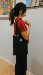 A person carrying a black dog mat folded into a shoulder tote bag with a small white label of brand Boop Boop Berlin