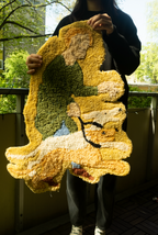Person holding a textured, multicolored rug outdoors
